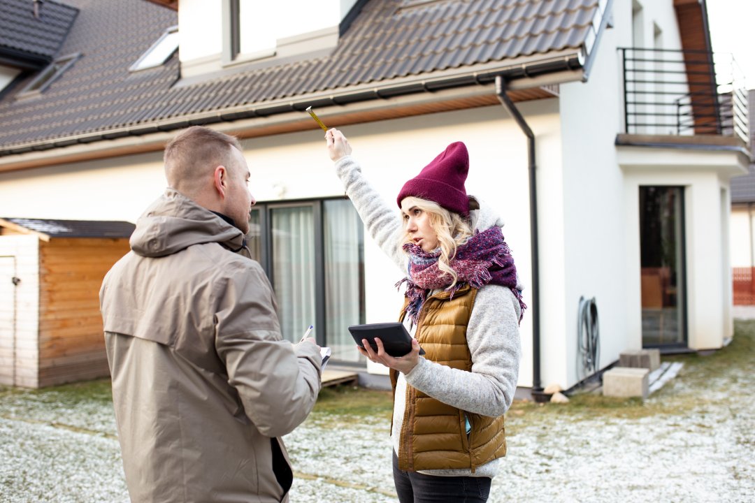 Portrait of two people dark-hared man back and blonde hair woman face with calculator holding pencil in air near house. Waving hands and argue speak to each other. Together. Side view light day.