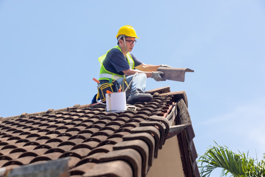 Worker man repairing eaves and tile of the old roof